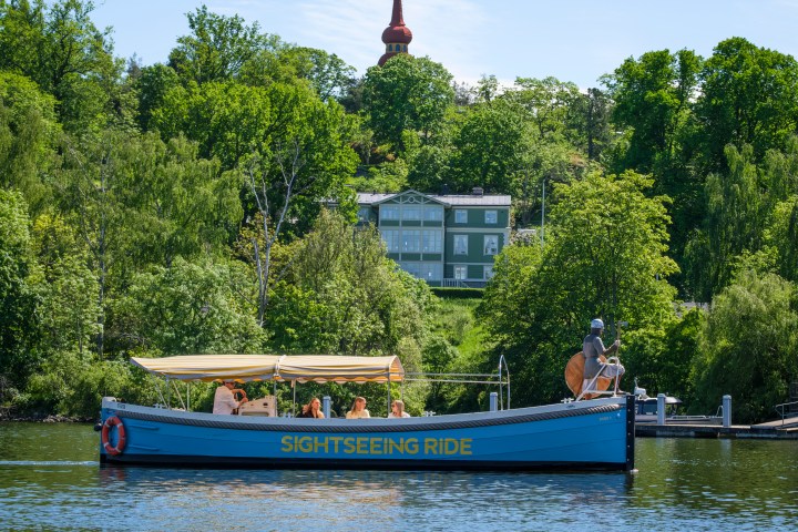 Tour boat on river with passengers, lush trees in background.