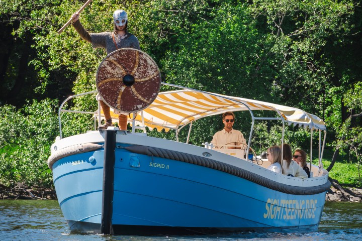 Boat with people on water, person in front dressed as a Viking with shield and helmet.